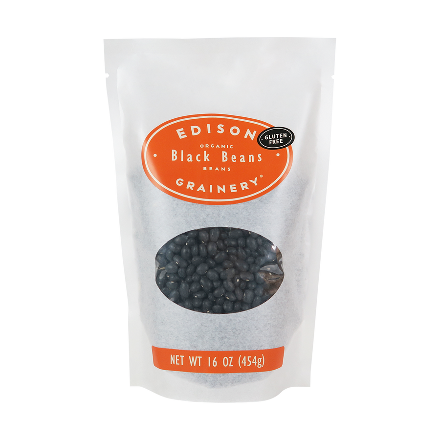 A 16 oz bag of Organic Black Beans standing upright in a bio-degradable bag. An orange oval label, bearing the product name sits above an oval viewing window revealing the product.