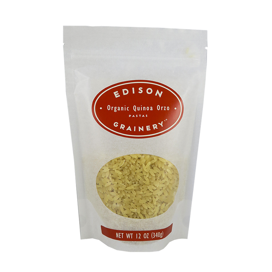 A 12 oz bag of Organic Quinoa Pasta: Orzo standing upright in a bio-degradable bag. A crimson red oval label, bearing the product name sits above an oval viewing window revealing the product.