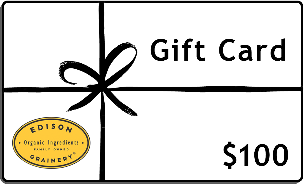 A white rectangular gift wrapped in a black ribbon with the words, Gift Card, $100 and a golden yellow logo superimposed atop it.
