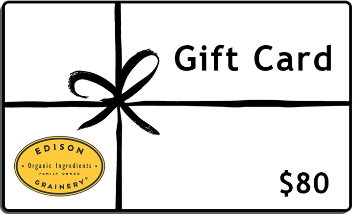 A white rectangular gift wrapped in a black ribbon with the words, Gift Card,  $80 and a golden yellow logo superimposed atop it.