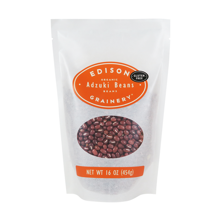 A 16 oz bag of Organic Adzuki Beans standing upright in a bio-degradable bag. An orange oval label, bearing the product name sits above an oval viewing window revealing the product.