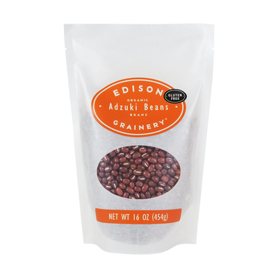 A 16 oz bag of Organic Adzuki Beans standing upright in a bio-degradable bag. An orange oval label, bearing the product name sits above an oval viewing window revealing the product.