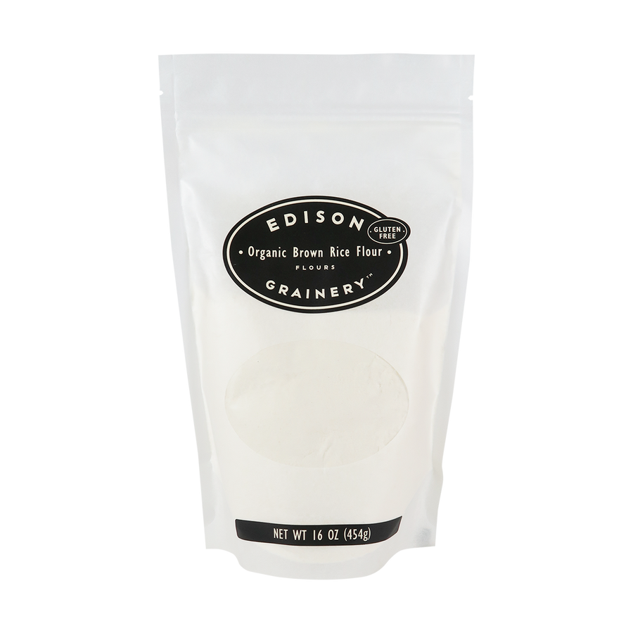A 16 oz bag of Organic Brown Rice Flour standing upright in a bio-degradable bag. A black oval label, bearing the product name sits above an oval viewing window revealing the product.