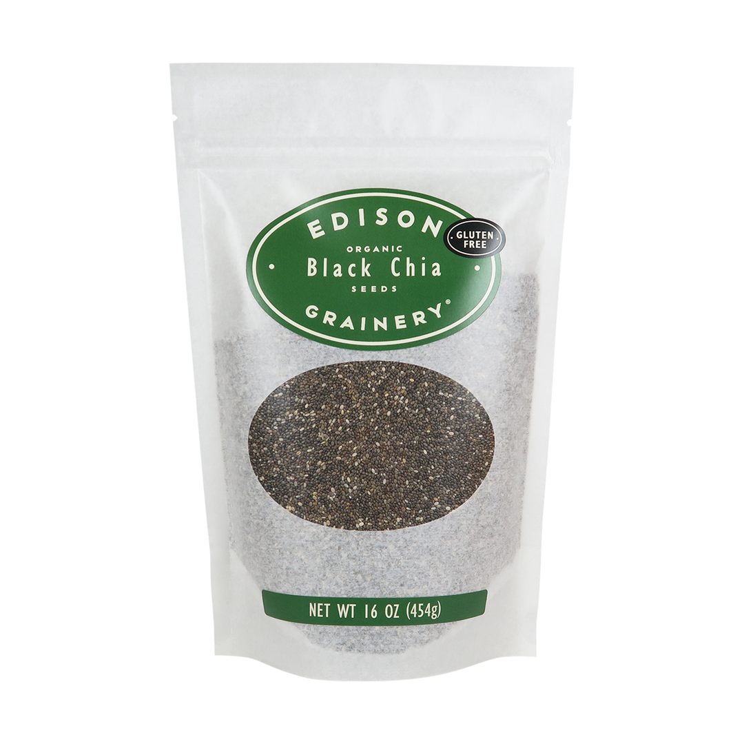 A 16 oz bag of Organic Black Chia Seeds standing upright in a bio-degradable bag. A forest green oval label, bearing the product name sits above an oval viewing window revealing the product.