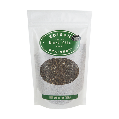 A 16 oz bag of Organic Black Chia Seeds standing upright in a bio-degradable bag. A forest green oval label, bearing the product name sits above an oval viewing window revealing the product.