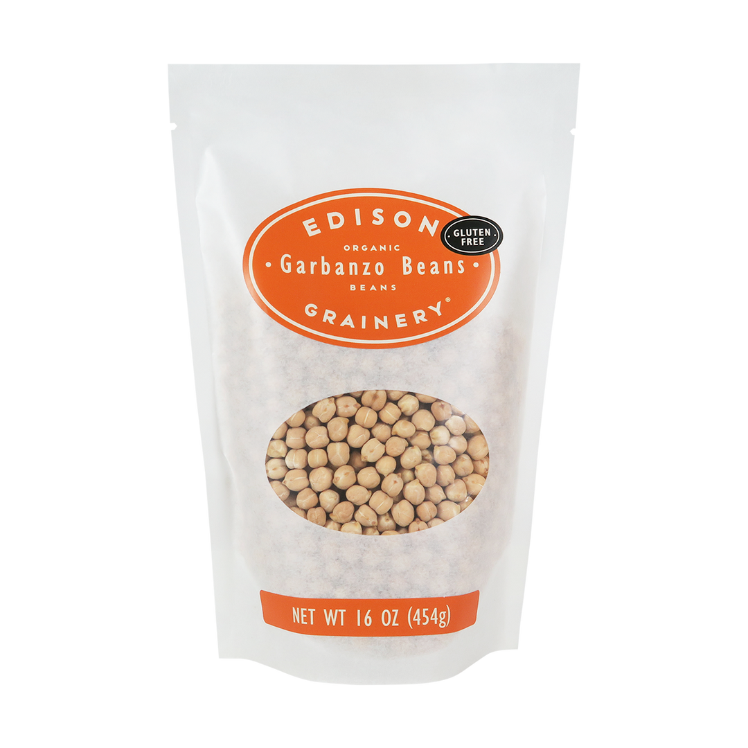 A 16 oz bag of Organic Garbanzo Beans standing upright in a bio-degradable bag. An orange oval label, bearing the product name sits above an oval viewing window revealing the product.