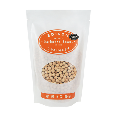 A 16 oz bag of Organic Garbanzo Beans standing upright in a bio-degradable bag. An orange oval label, bearing the product name sits above an oval viewing window revealing the product.