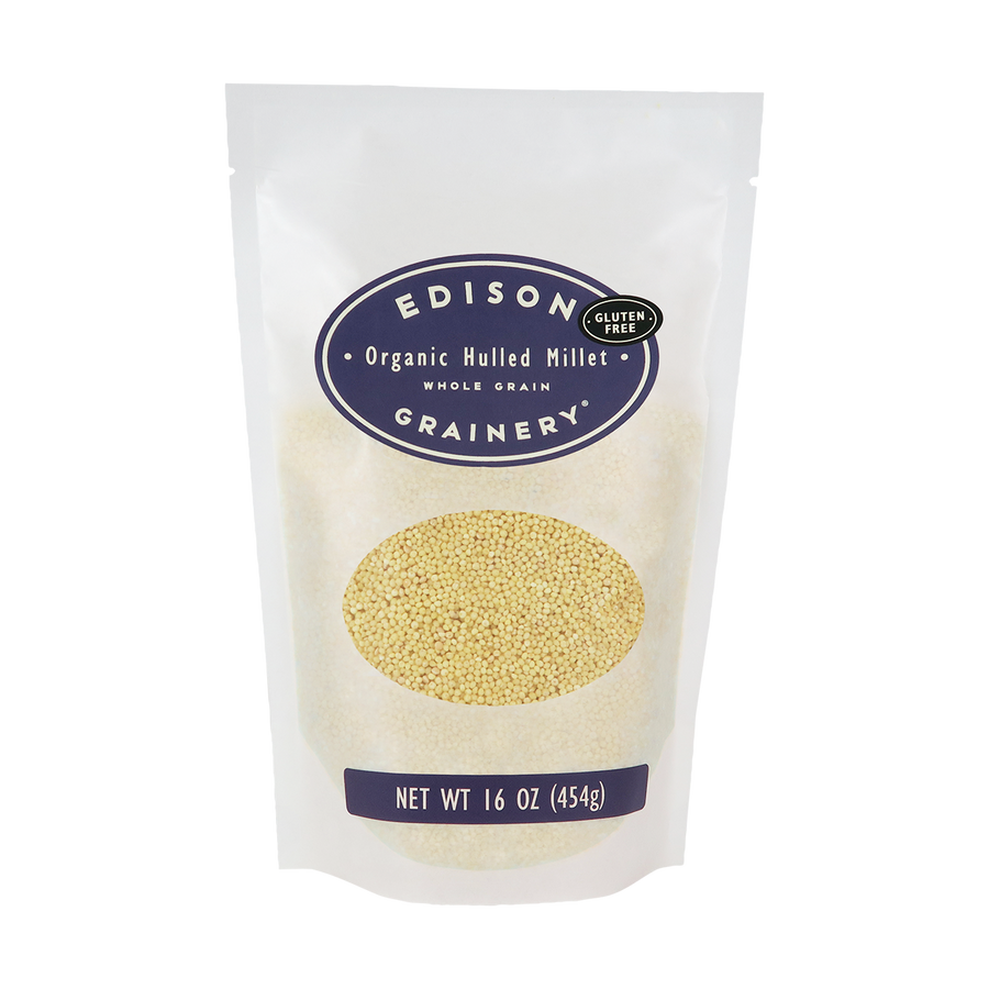 A 16 oz bag of Organic Hulled Millet standing upright in a bio-degradable bag. A deep purple oval label, bearing the product name sits above an oval viewing window revealing the product.