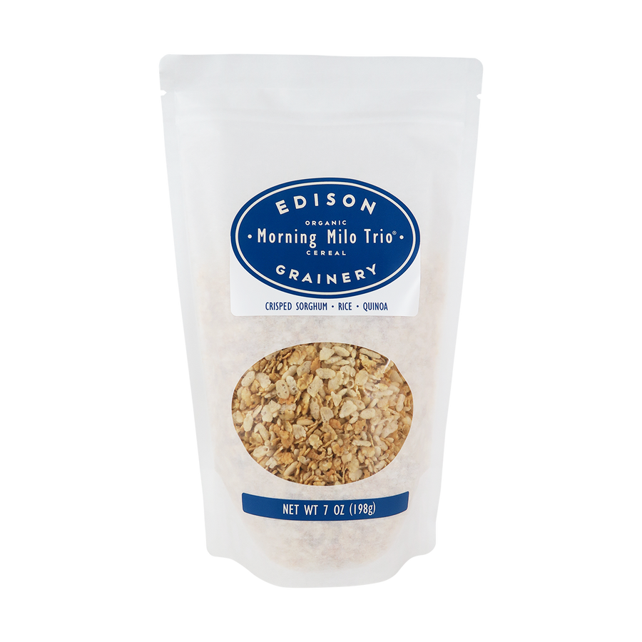 A 7 oz bag of Organic Morning Milo Trio Cereal standing upright in a bio-degradable bag. A royal blue, oval label bearing the product name sits above an oval viewing window revealing the product.