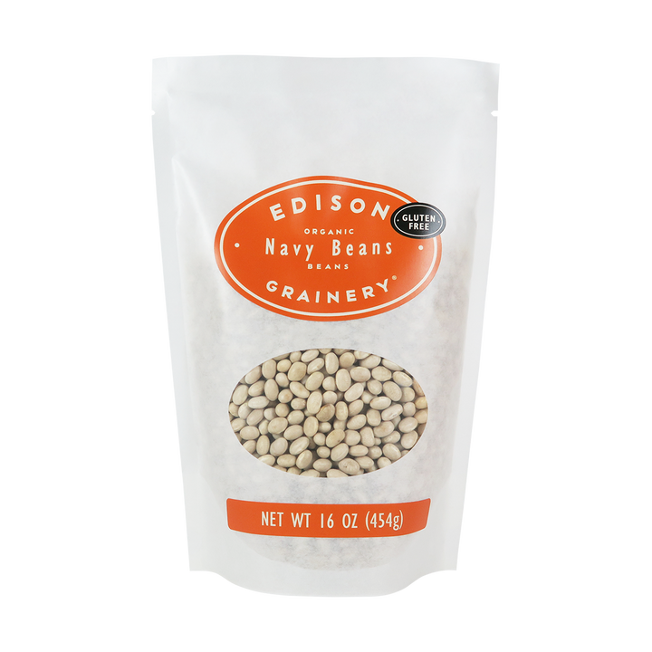 A 16 oz bag of Organic Navy Beans standing upright in a bio-degradable bag. An orange oval label, bearing the product name sits above an oval viewing window revealing the product.