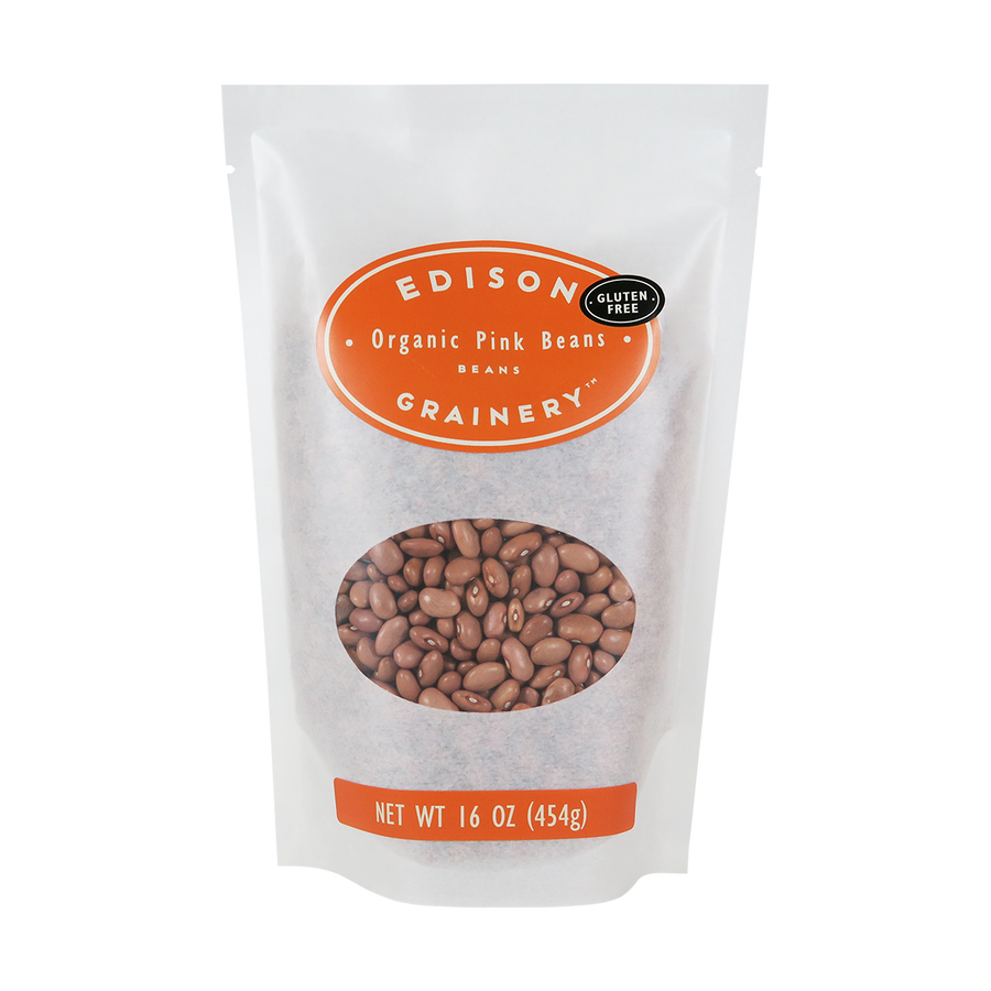 A 16 oz bag of Organic Pink Beans standing upright in a bio-degradable bag. An orange oval label, bearing the product name sits above an oval viewing window revealing the product.