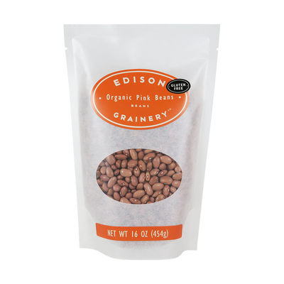 A 16 oz bag of Organic Pink Beans standing upright in a bio-degradable bag. An orange oval label, bearing the product name sits above an oval viewing window revealing the product.
