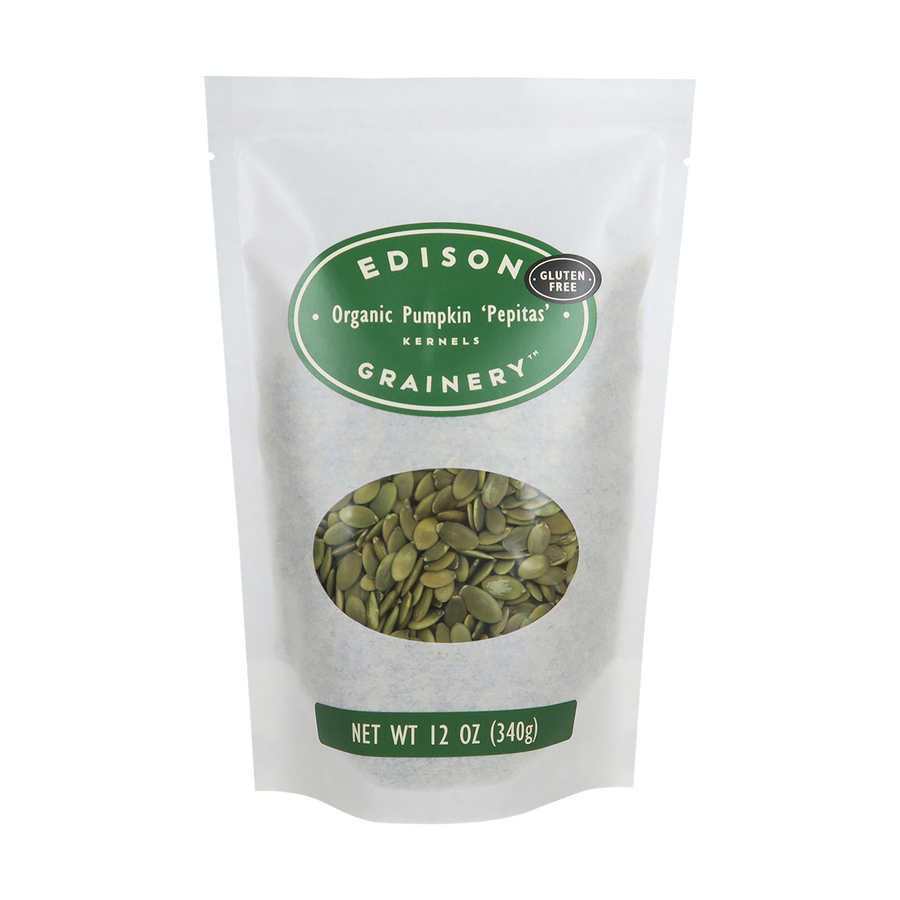 A 12 oz bag of Organic Pumpkin 'Pepitas" standing upright in a bio-degradable bag. A forest green oval label, bearing the product name sits above an oval viewing window revealing the product.