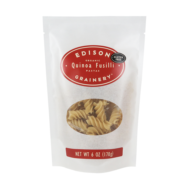A 6 oz bag of Organic Quinoa Pasta: Fusilli standing upright in a bio-degradable bag. A crimson red oval label, bearing the product name sits above an oval viewing window revealing the product.