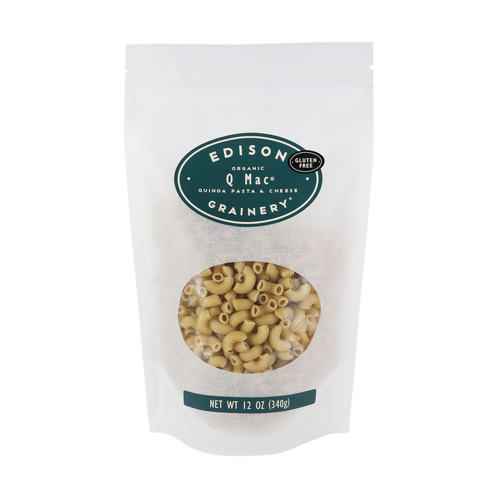 A 12oz bag of Organic Q-Mac standing upright in a bio-degradable bag. A dark teal oval label, bearing the product name sits above an oval viewing window revealing the product.