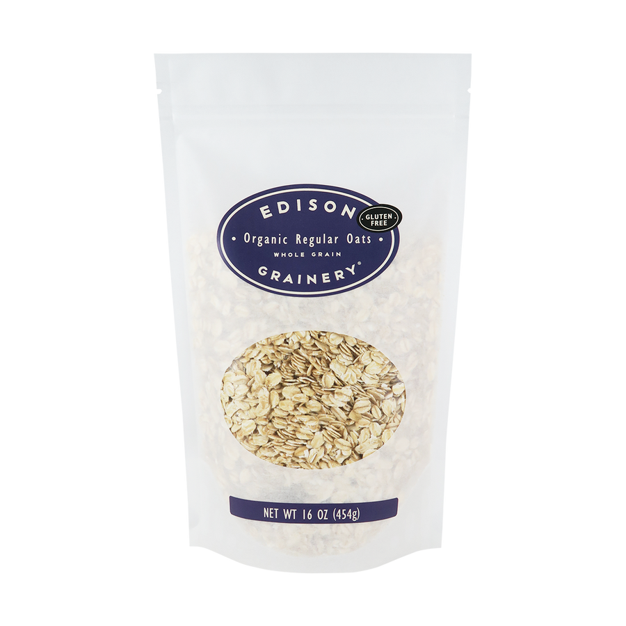 A 16 oz bag of Organic Regular Rolled Oats standing upright in a bio-degradable bag. A deep purple oval label, bearing the product name sits above an oval viewing window revealing the product.