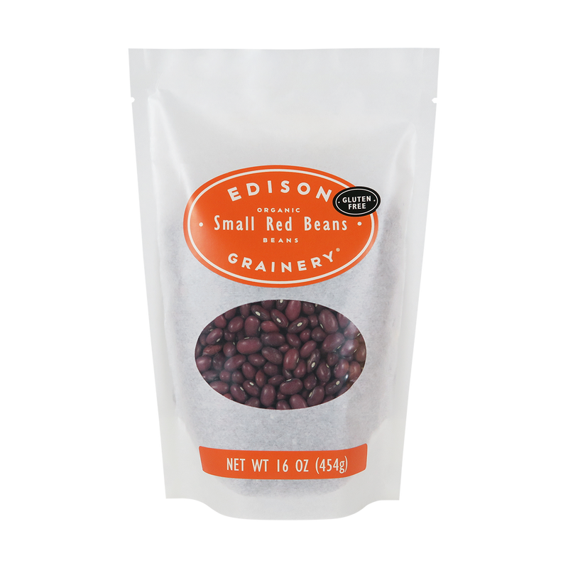 A 16 oz bag of Organic Small Red Beans standing upright in a bio-degradable bag. An orange oval label, bearing the product name sits above an oval viewing window revealing the product.