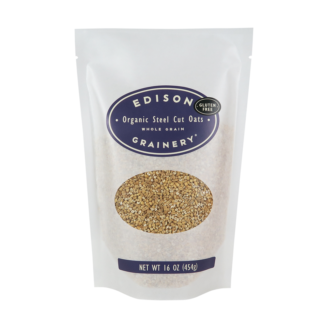 A 16 oz bag of Organic Steel Cut Oats standing upright in a bio-degradable bag. A deep purple oval label, bearing the product name sits above an oval viewing window revealing the product.