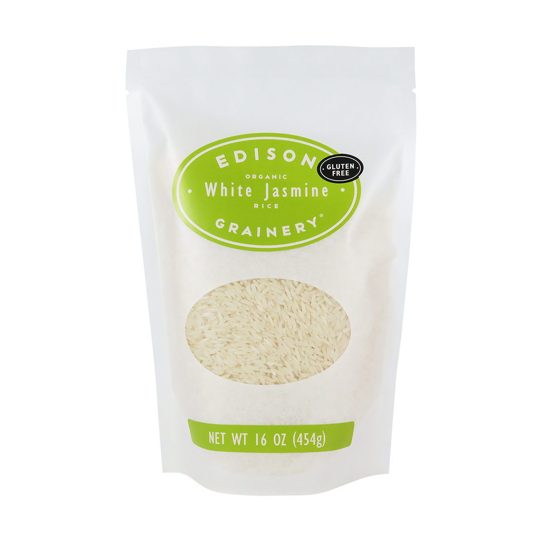 A 16 oz bag of Organic White Jasmine Rice standing upright in a bio-degradable bag. A lime-green oval label, bearing the product name sits above an oval viewing window revealing the product.
