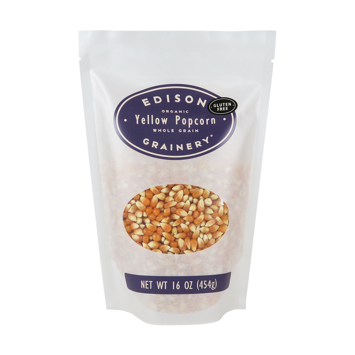 A 16 oz bag of Organic Yellow Popcorn standing upright in a bio-degradable bag. A deep purple oval label, bearing the product name sits above an oval viewing window revealing the product.