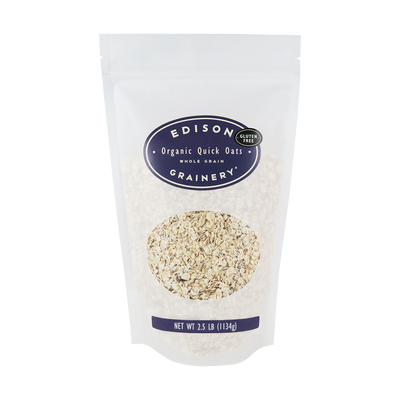 A 2.5 lb bag of Organic Quick Oats standing upright in a bio-degradable bag. A deep purple oval label, bearing the product name sits above an oval viewing window revealing the product.