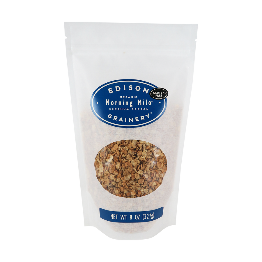 A 8 oz bag of Organic Morning Milo Cereal standing upright in a bio-degradable bag. A royal blue, oval label bearing the product name sits above an oval viewing window revealing the product.