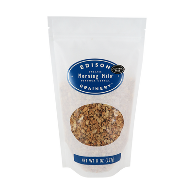 A 8 oz bag of Organic Morning Milo Cereal standing upright in a bio-degradable bag. A royal blue, oval label bearing the product name sits above an oval viewing window revealing the product.