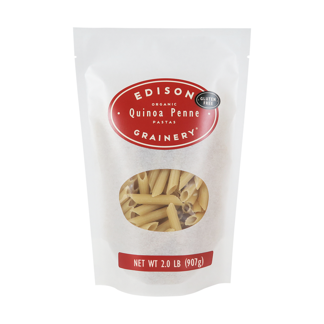 A 2 lb bag of Organic Quinoa Pasta: Penne standing upright in a bio-degradable bag. A crimson red oval label, bearing the product name sits above an oval viewing window revealing the product.