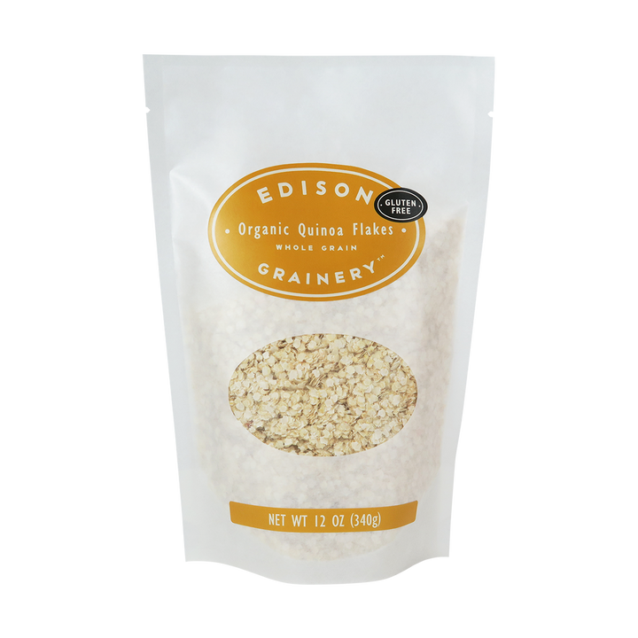 A 12 oz bag of Organic Quinoa Flakes standing upright in a bio-degradable bag. A golden yellow, oval label bearing the product name sits above an oval viewing window revealing the product.