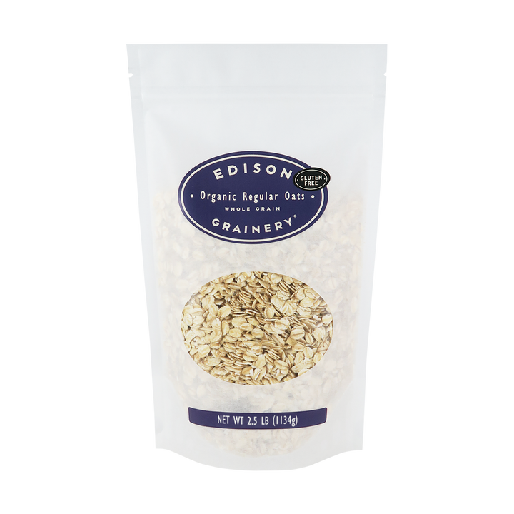 A 2.5 lb bag of Organic Regular Rolled Oats standing upright in a bio-degradable bag. A deep purple oval label, bearing the product name sits above an oval viewing window revealing the product.